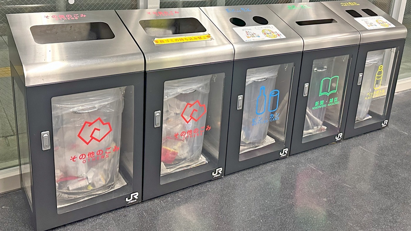 A row of sorted bins on a Japanese station concourse, one opening per category